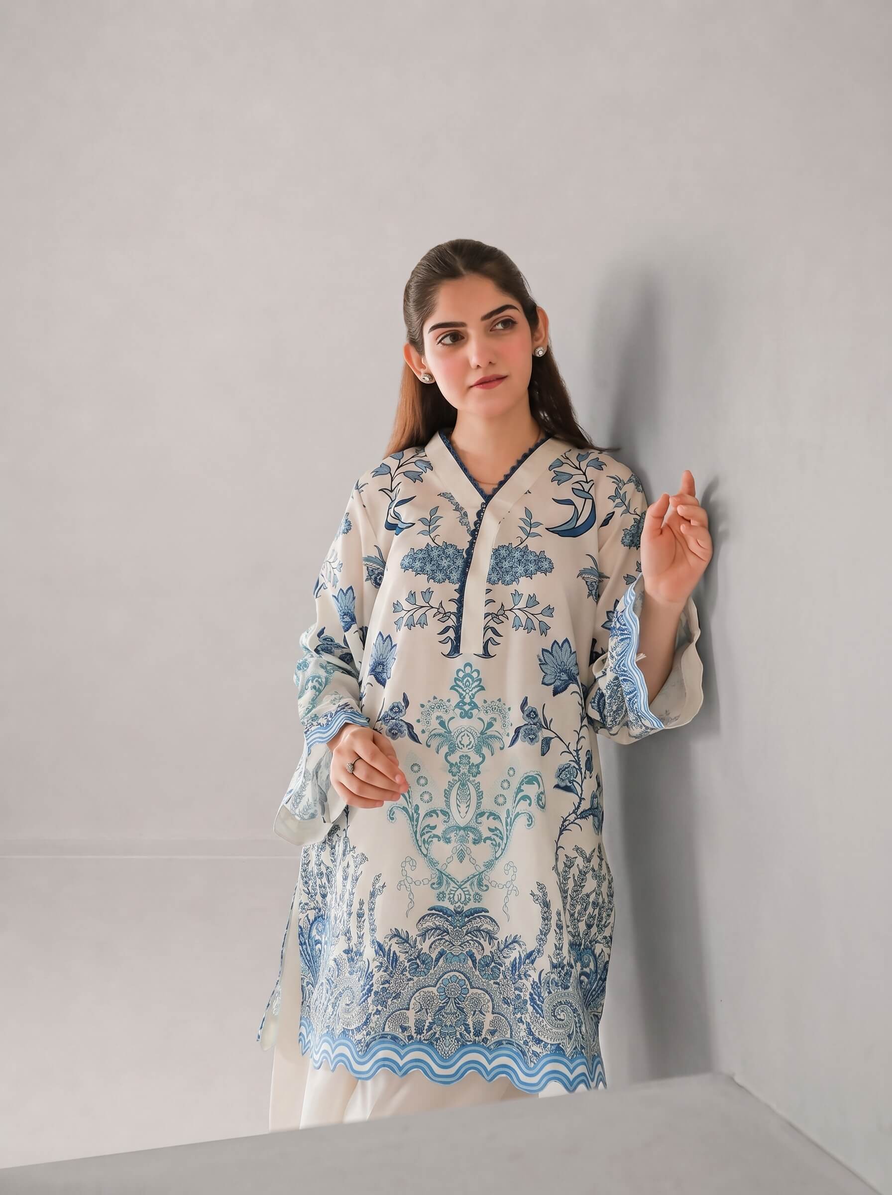 A woman modeling a cream-colored kurta with blue floral and wave patterns, standing against a light gray wall.