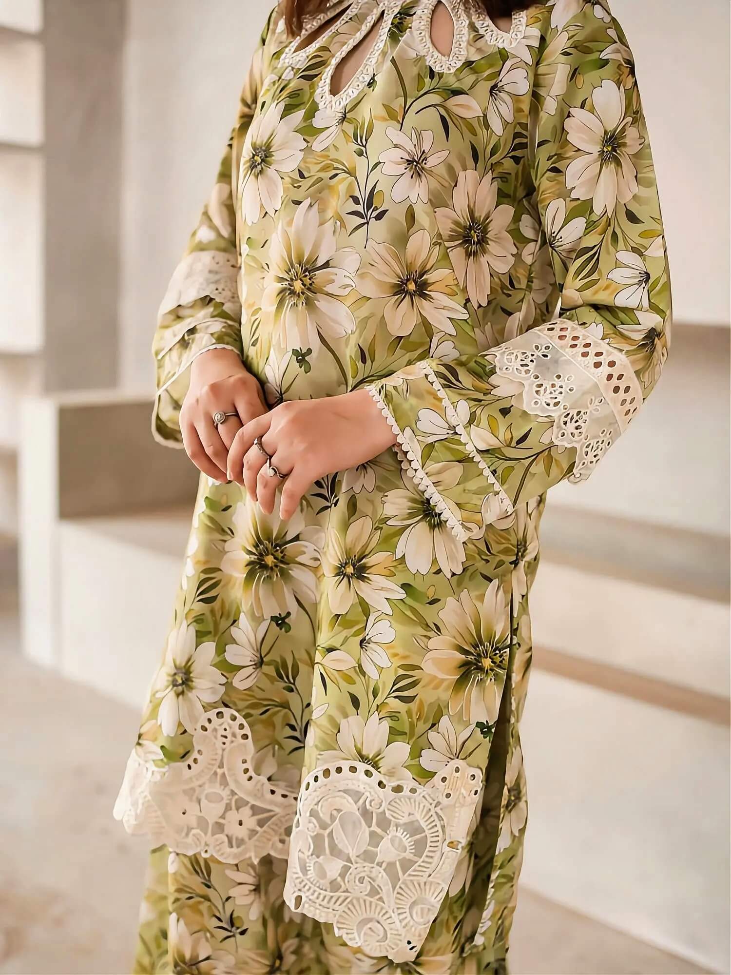 A woman wearing a long-sleeve floral tunic dress with cream lace trim, featuring a green, beige, and white daisy pattern.