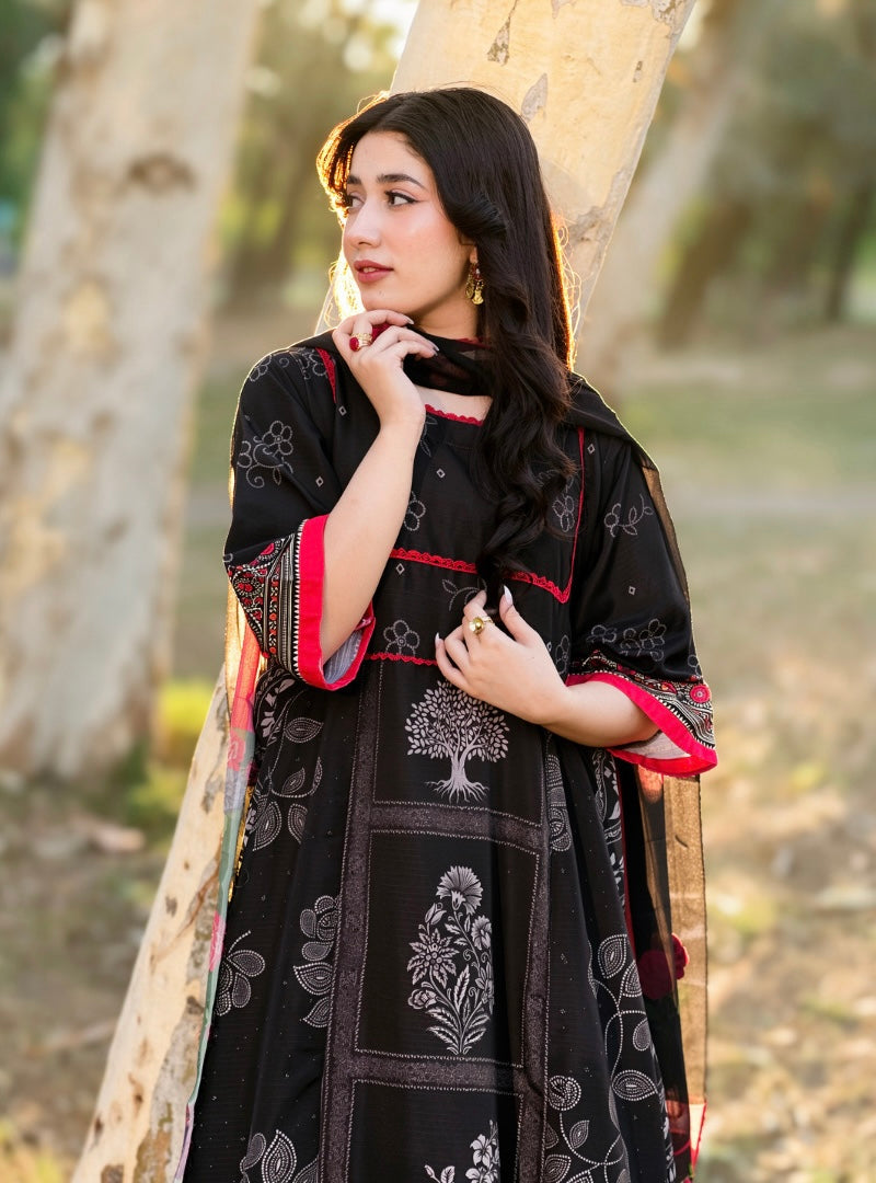 A woman wearing a black printed kurta with red and white border details, standing outdoors against a blurred tree trunk background.