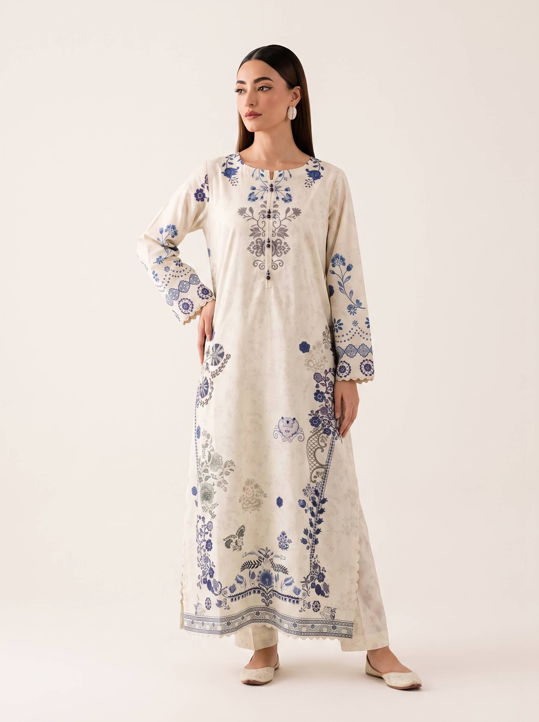 A woman modeling a long cream-colored kurta with blue floral and botanical embroidery, standing against a plain off-white studio background.