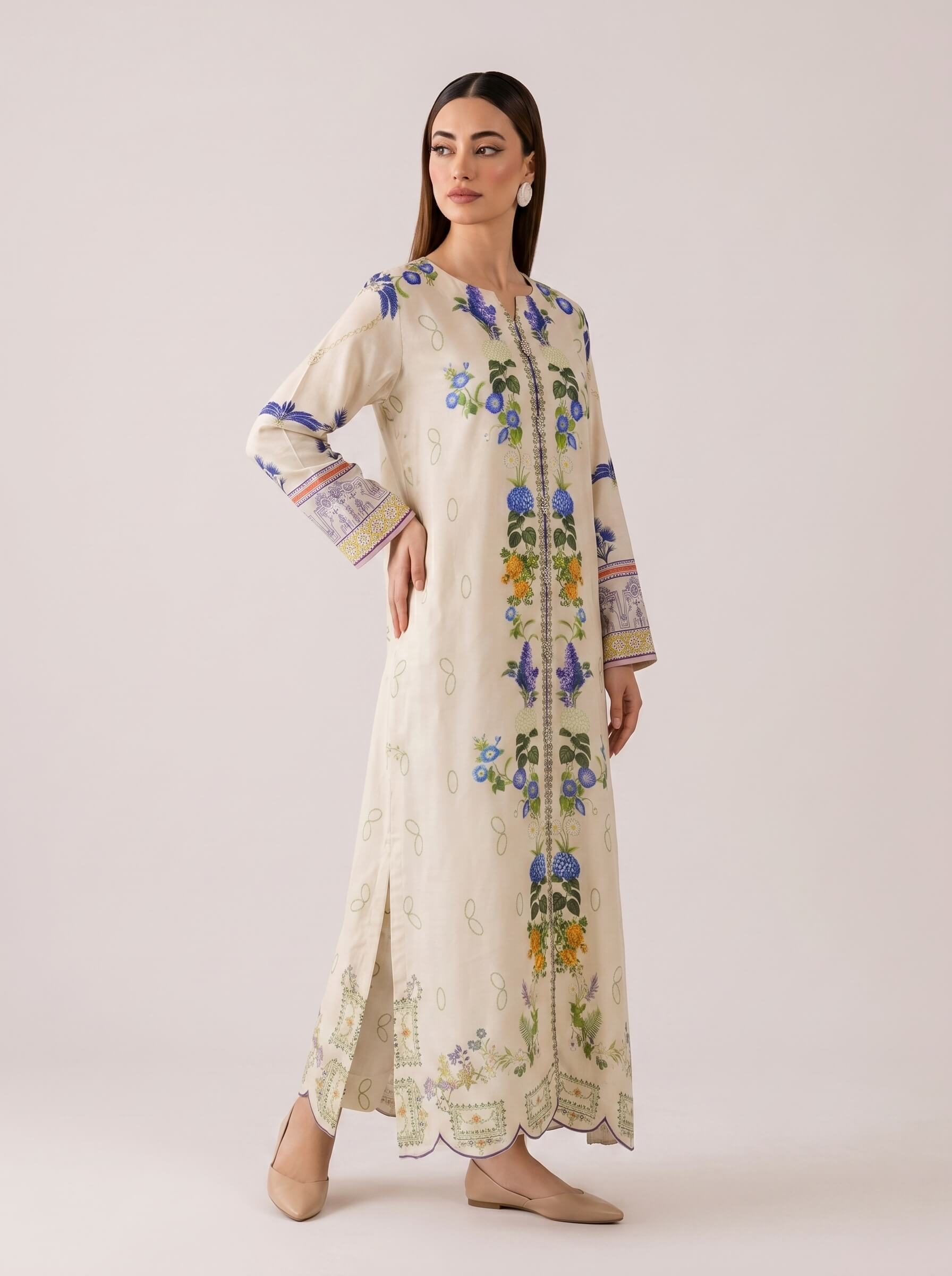 A woman modeling a long cream-colored embroidered kurta with blue, green, and yellow floral patterns, standing against a solid light beige studio background.
