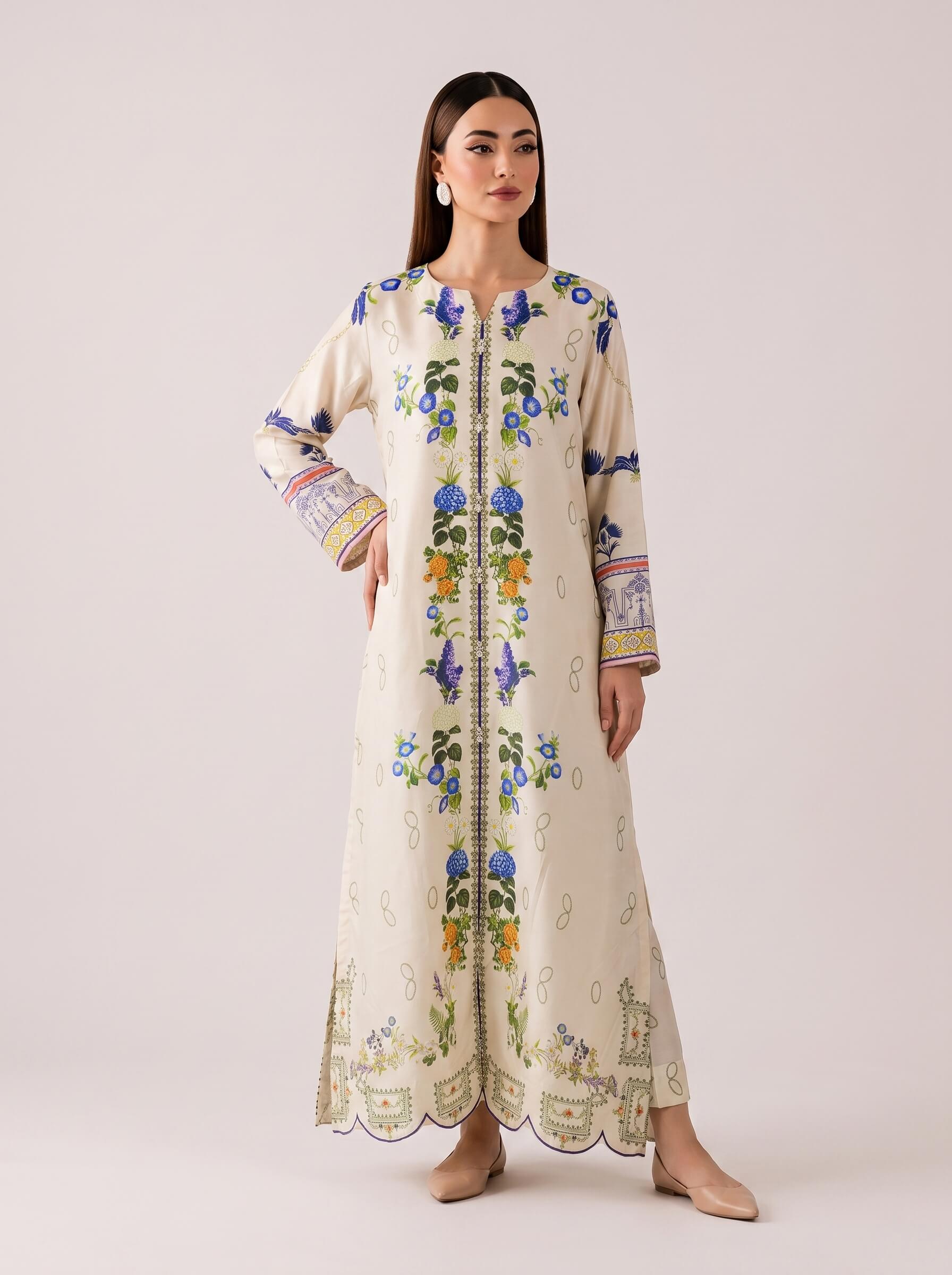 A woman modeling a long cream-colored embroidered kurta with blue, green, and yellow floral patterns, standing against a solid light beige background.