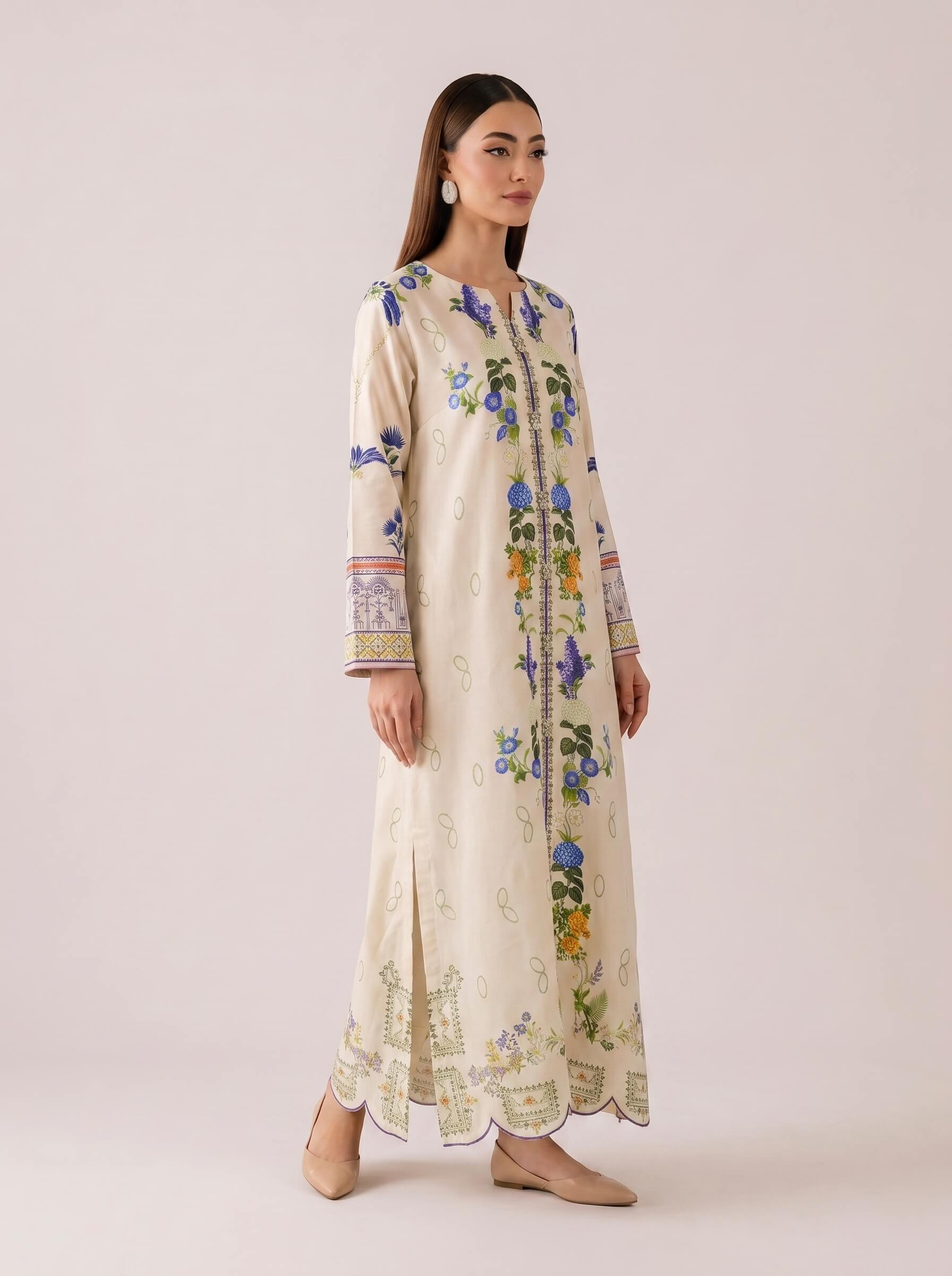 A woman modeling a long cream-colored embroidered kurta with blue, green, and yellow floral patterns, standing against a solid light beige studio background.