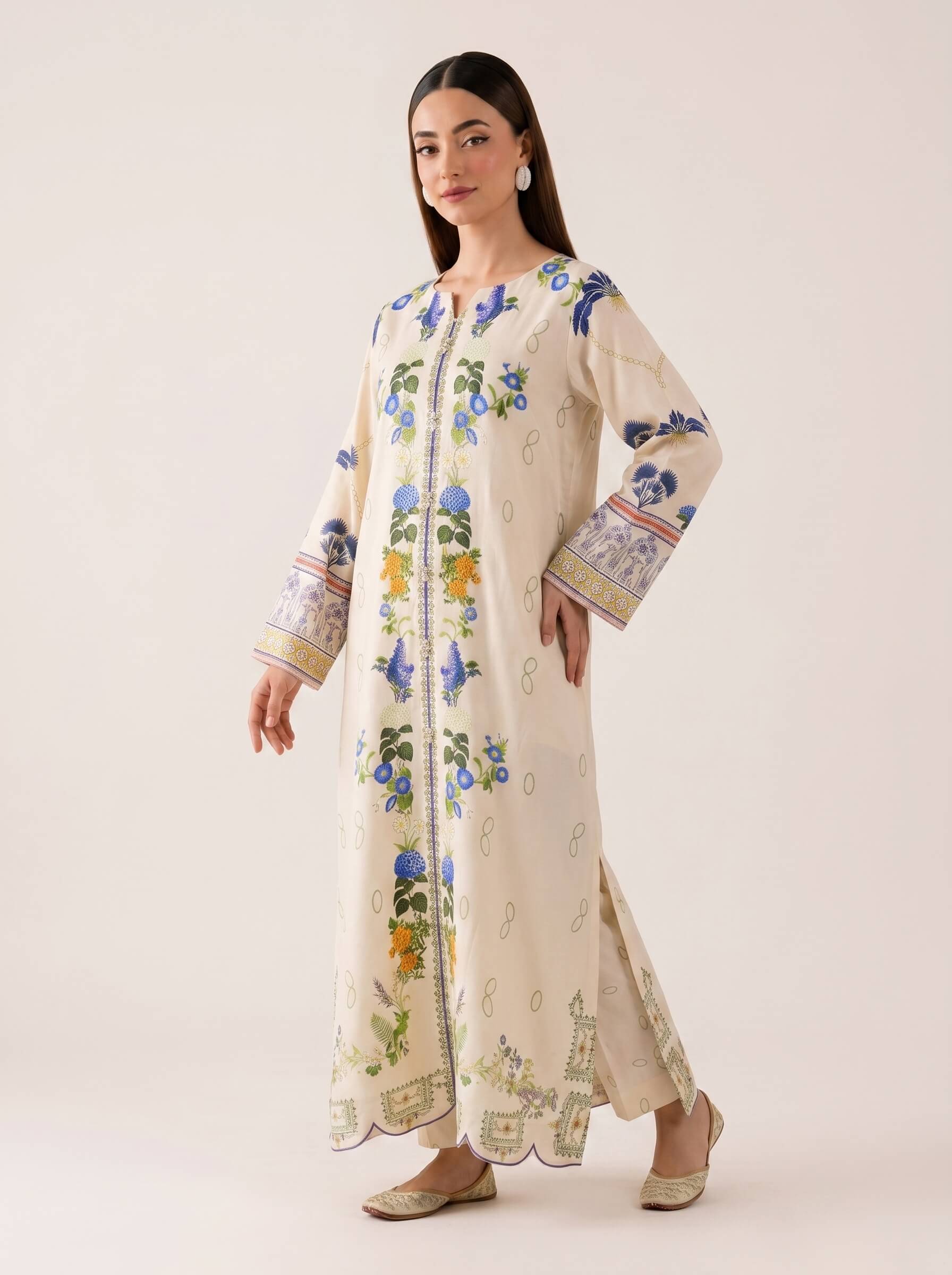 A woman modeling a long cream-colored embroidered kurta with blue, green, and yellow floral motifs and patterned cuffs, photographed against a plain light beige studio background.