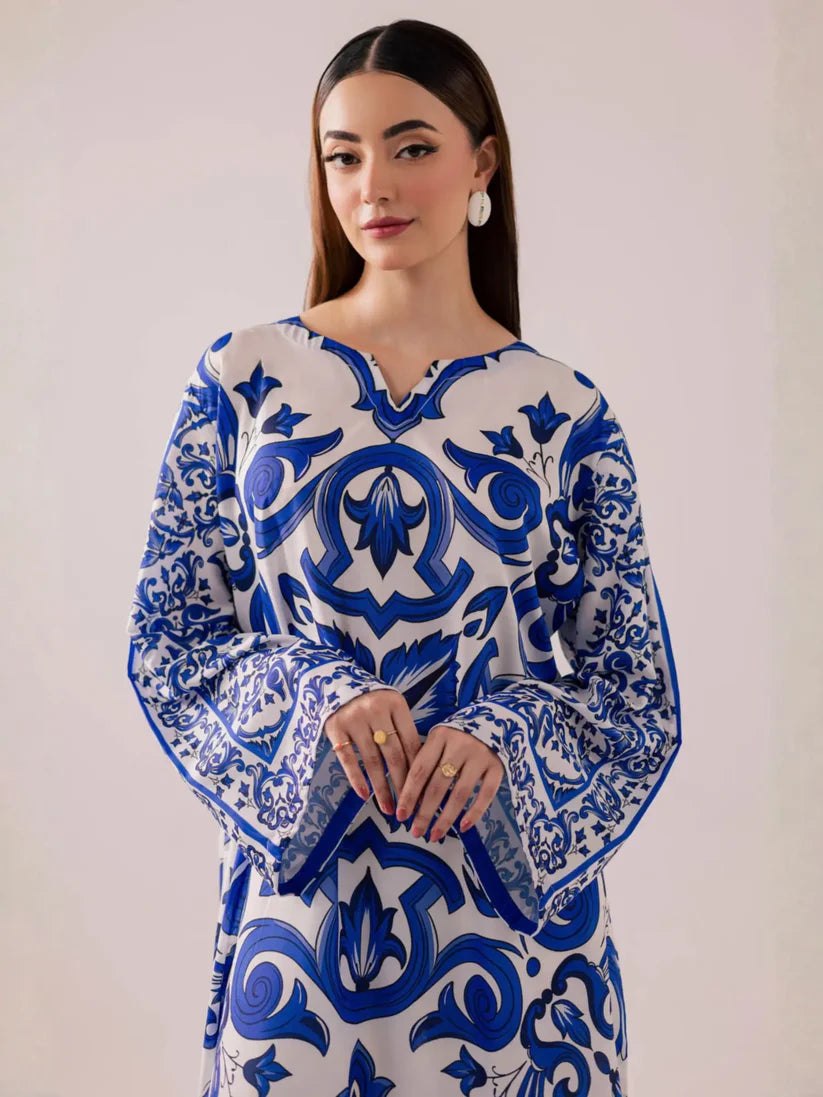 A woman modeling a long-sleeved tunic dress with a blue and white baroque-style floral pattern against a plain light beige background.