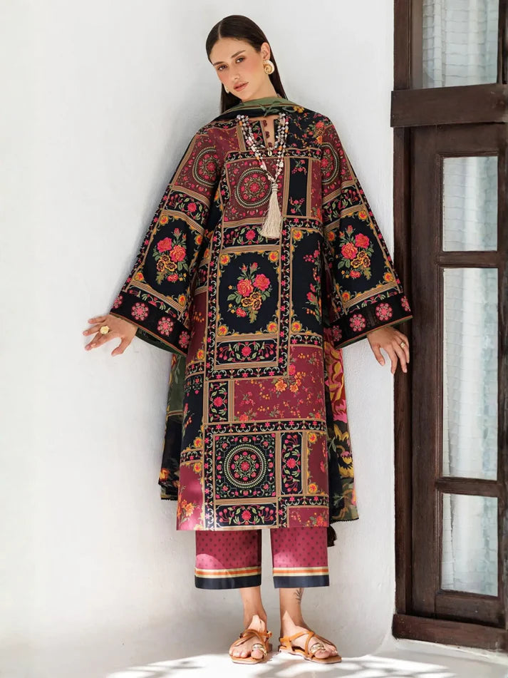 A woman models a traditional South Asian outfit consisting of a long-sleeved kurta and matching cropped trousers. The outfit features a highly detailed, multicolor patchwork print with floral motifs, geometric borders, and dark backgrounds, paired with a green dupatta and gold jewelry.