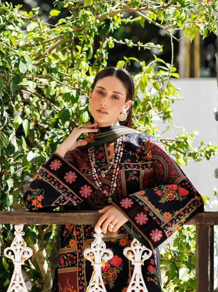 A woman wearing a black embroidered kurta with colorful floral patterns, posing outdoors on a balcony with green foliage in the background.