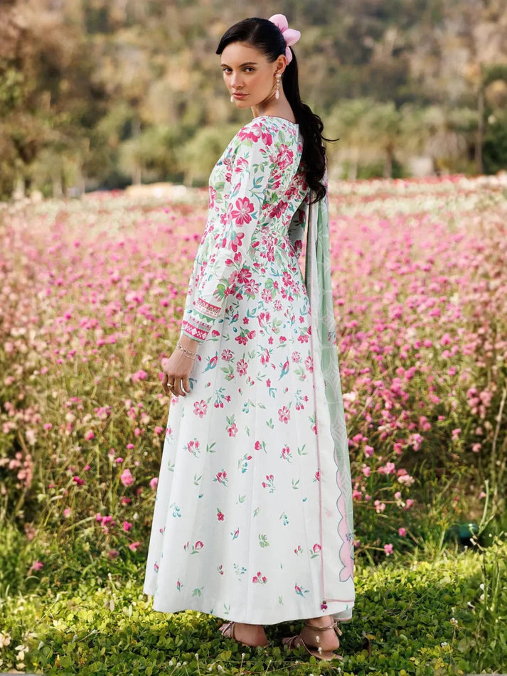 A woman stands in a field of pink flowers wearing a long white printed dress with pink and green floral motifs and a matching sheer dupatta.