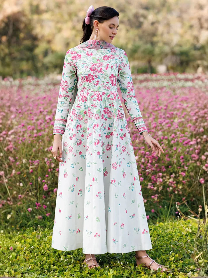 A woman wearing a long-sleeved white maxi dress with a pink and green floral print, standing in a field of pink flowers.